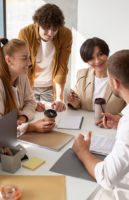 Four colleagues collaborate around a table during an office meeting with notebooks and coffee.